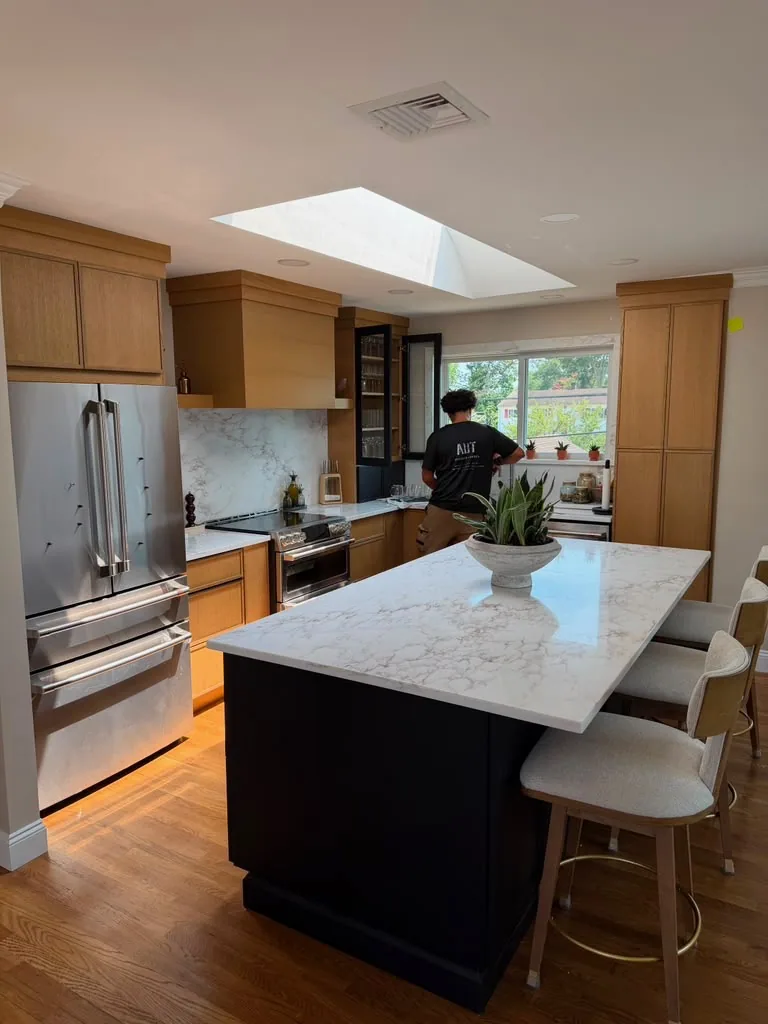 Warm wood kitchen cabinets with a dark island, white countertop and skylight