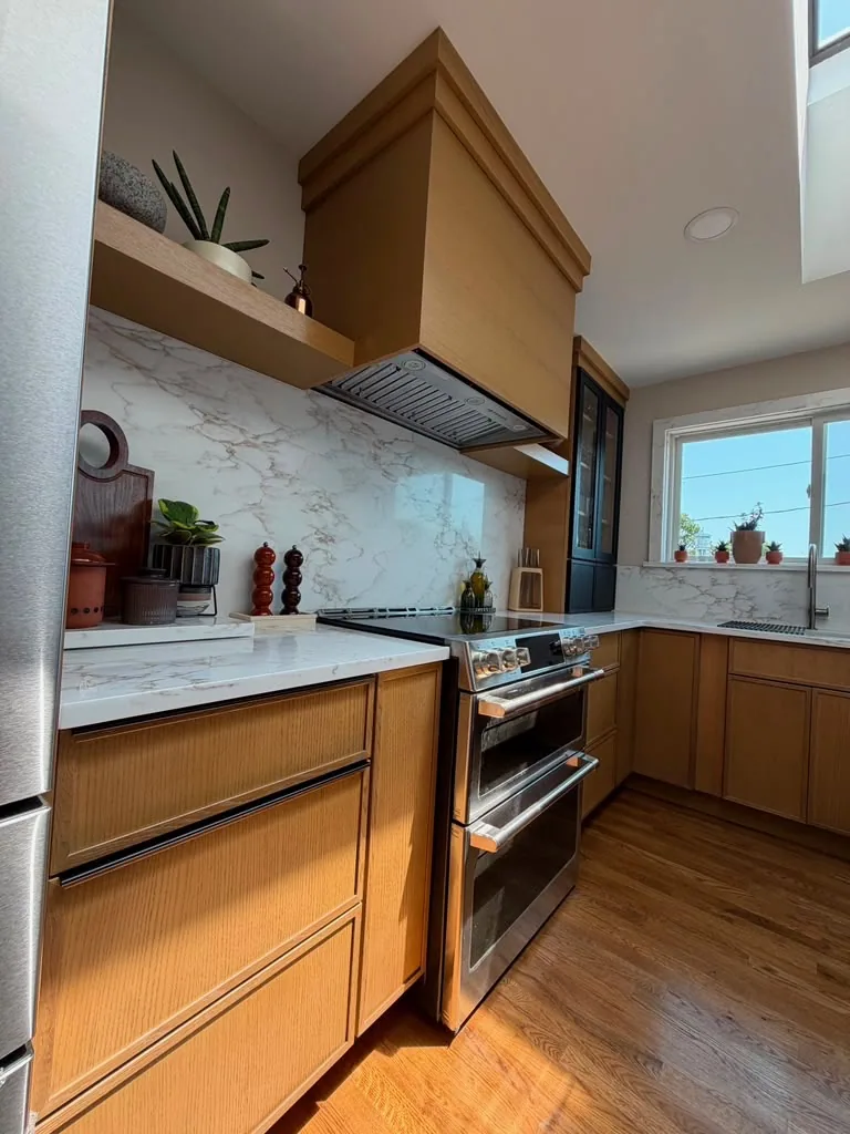 Wood range hood and marble backsplash above a stainless range in a warm wood kitchen
