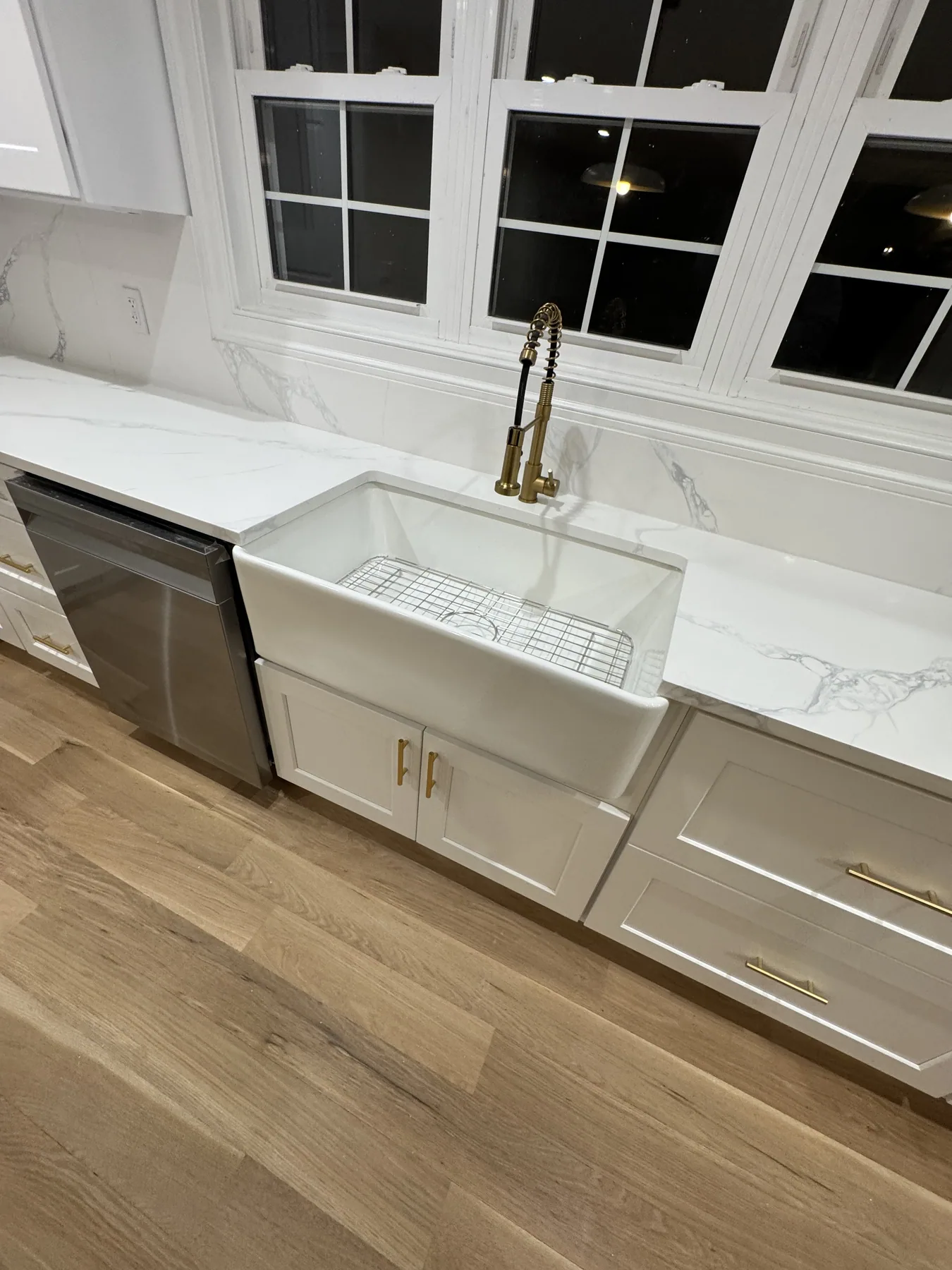 White farmhouse apron sink with a brass faucet and marble countertop