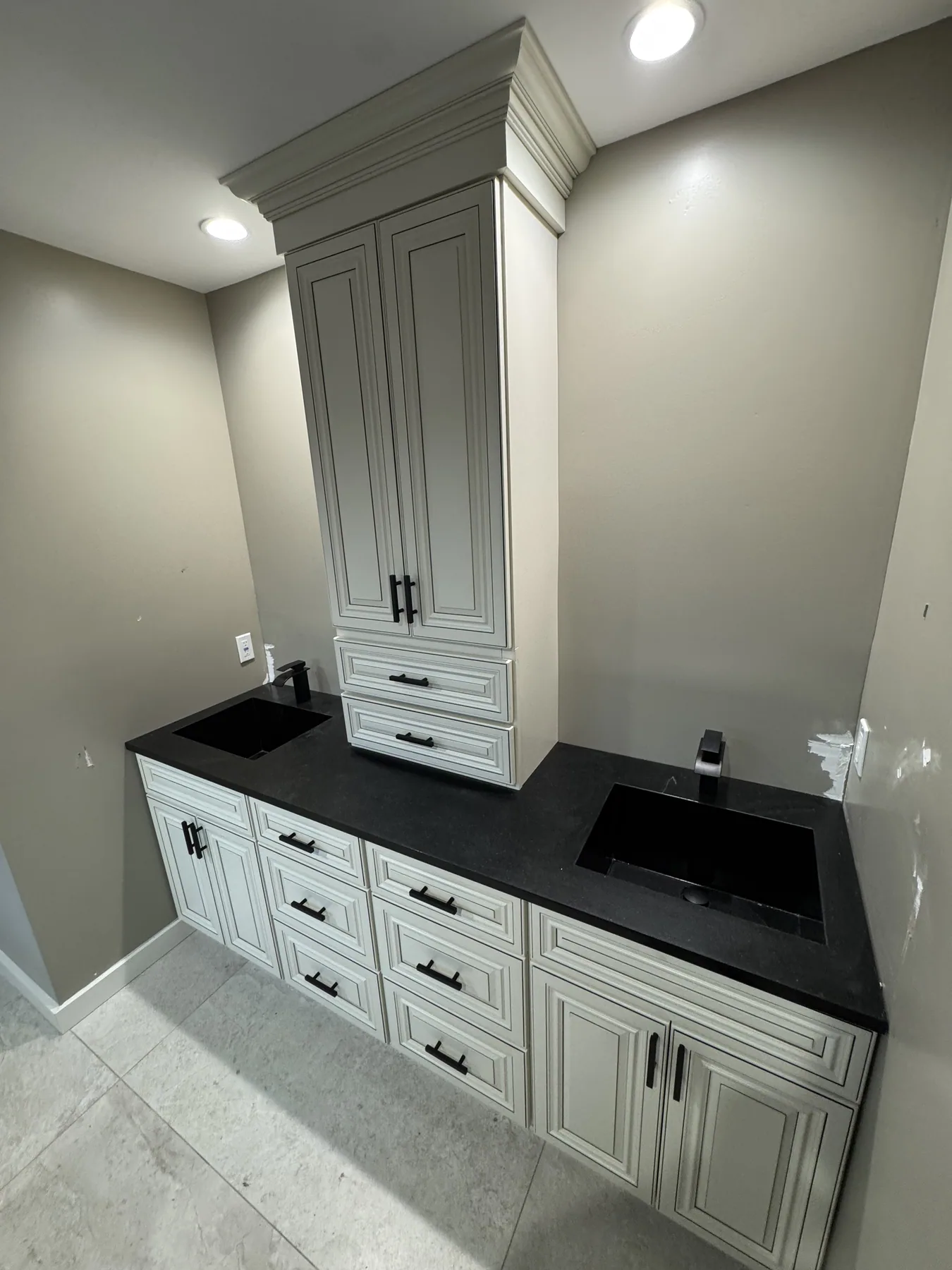 Cream vanity cabinetry with a black countertop, black sink and tall storage cabinet