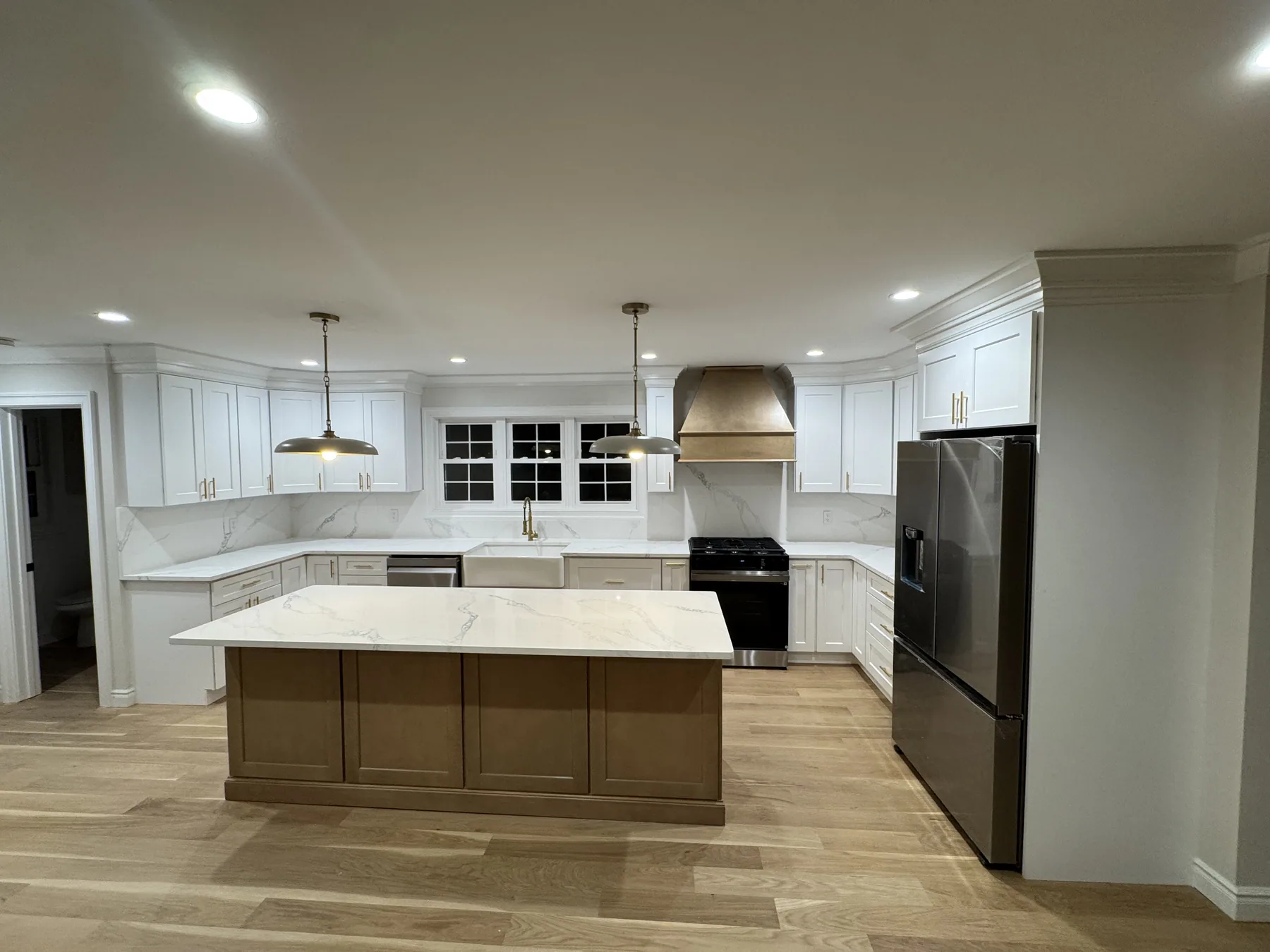 White shaker kitchen with a warm wood island and marble countertops under pendant lighting