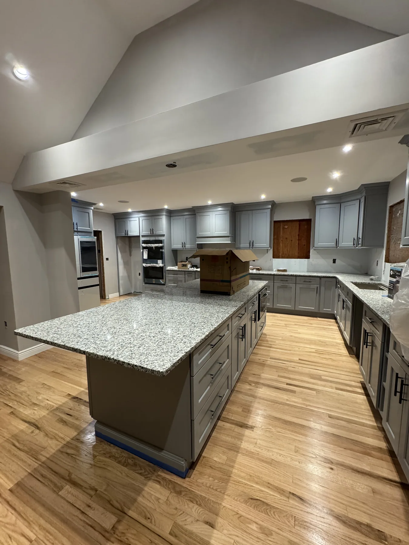 Wide view of a gray kitchen with a large granite island and hardwood floors