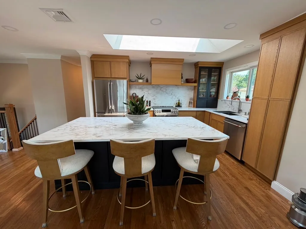 Warm wood kitchen with a dark island, marble countertop and upholstered counter stools
