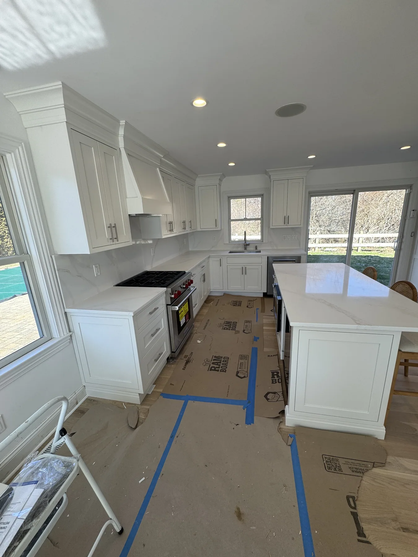 White kitchen in progress with protected floors, a marble island and cabinet hood surround
