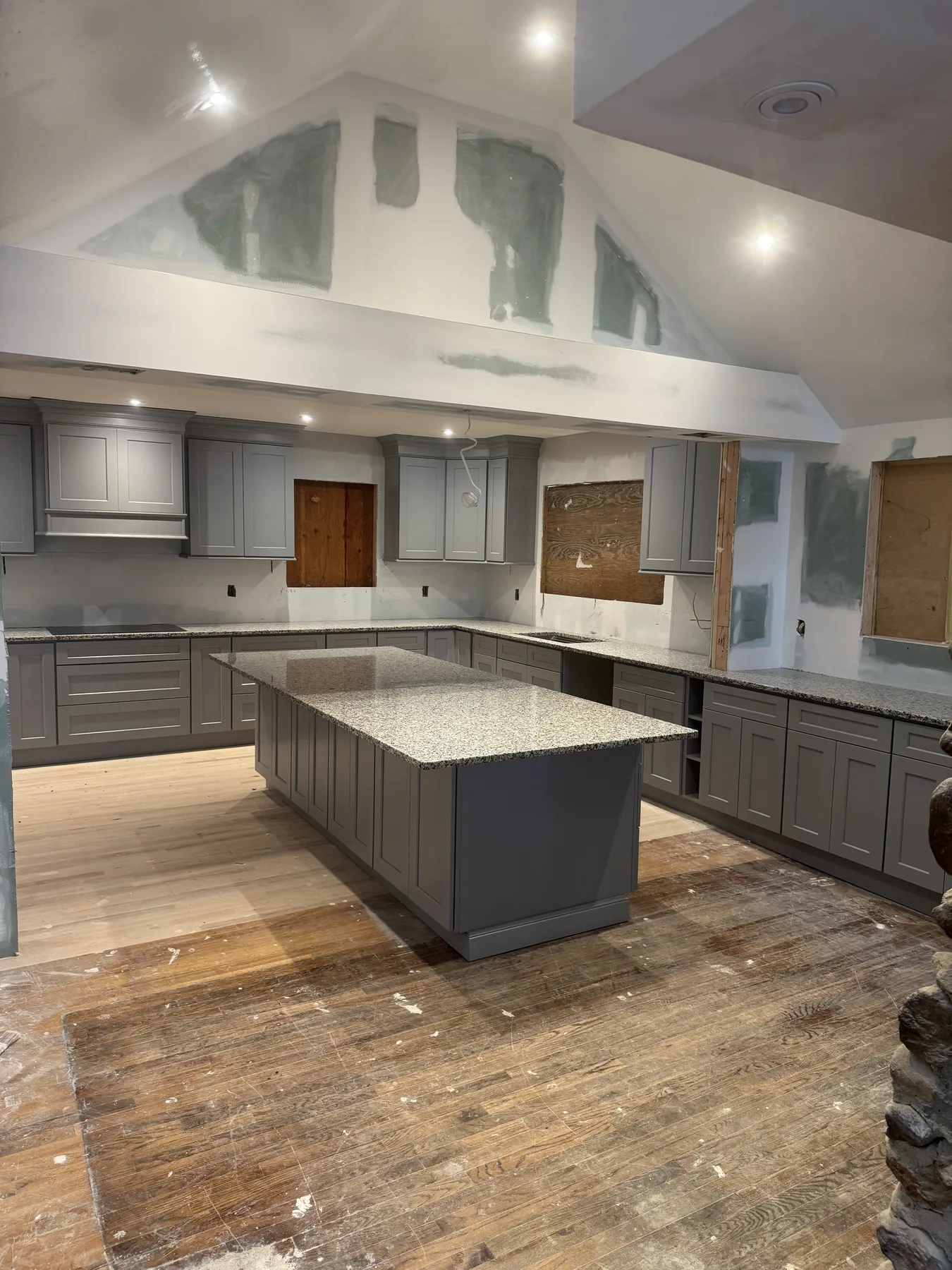 Gray kitchen cabinets with a granite island countertop under a vaulted ceiling
