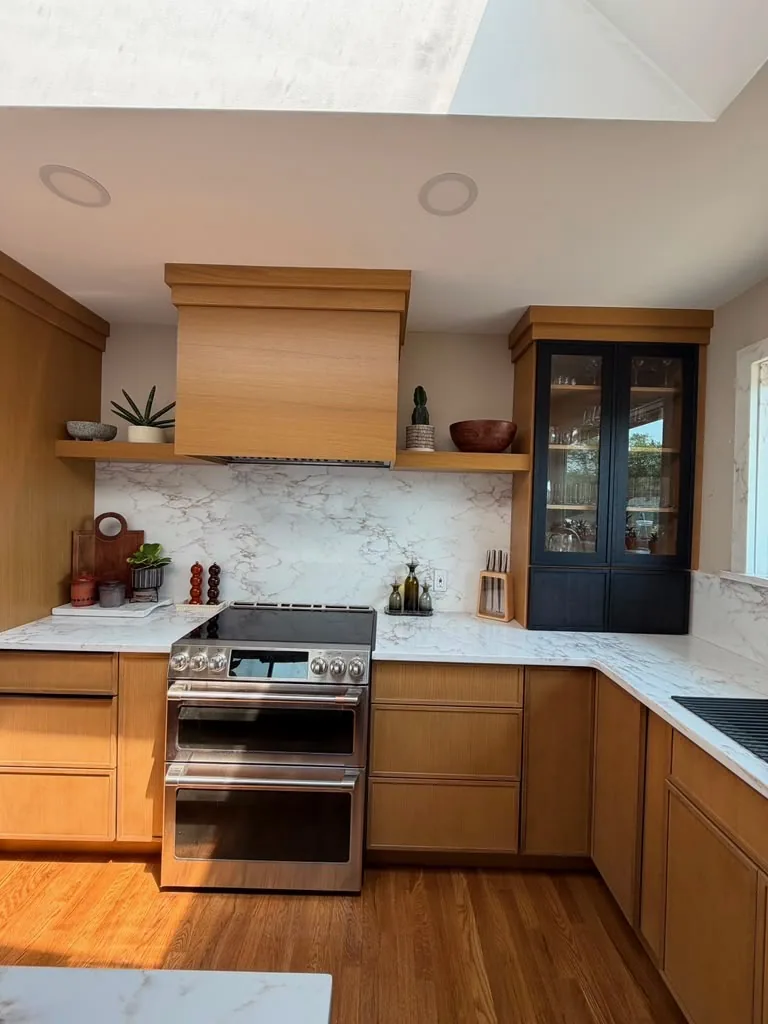 Warm wood kitchen cabinets with a range, wood hood and marble backsplash