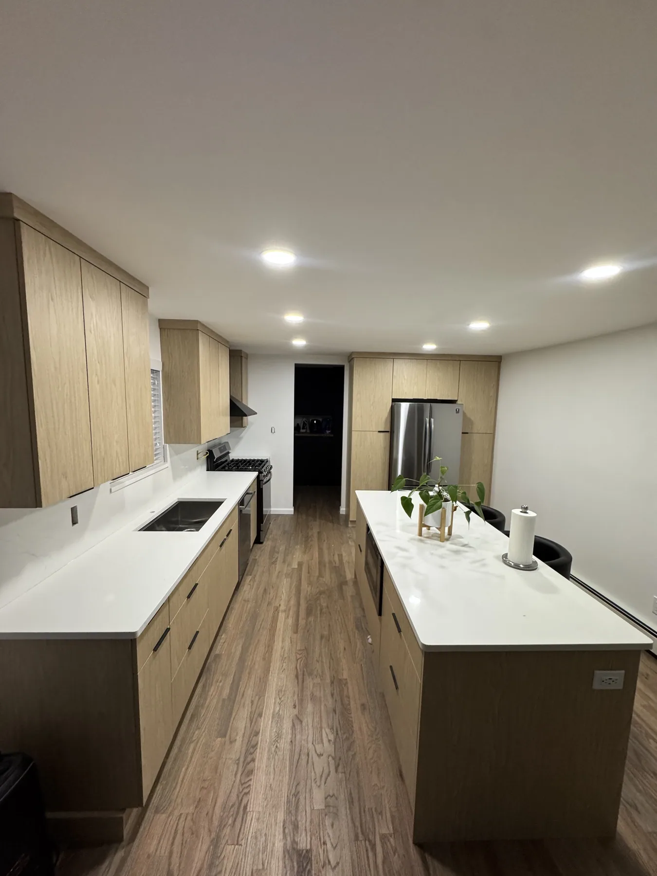 Natural wood kitchen cabinets with a white island countertop and wood flooring