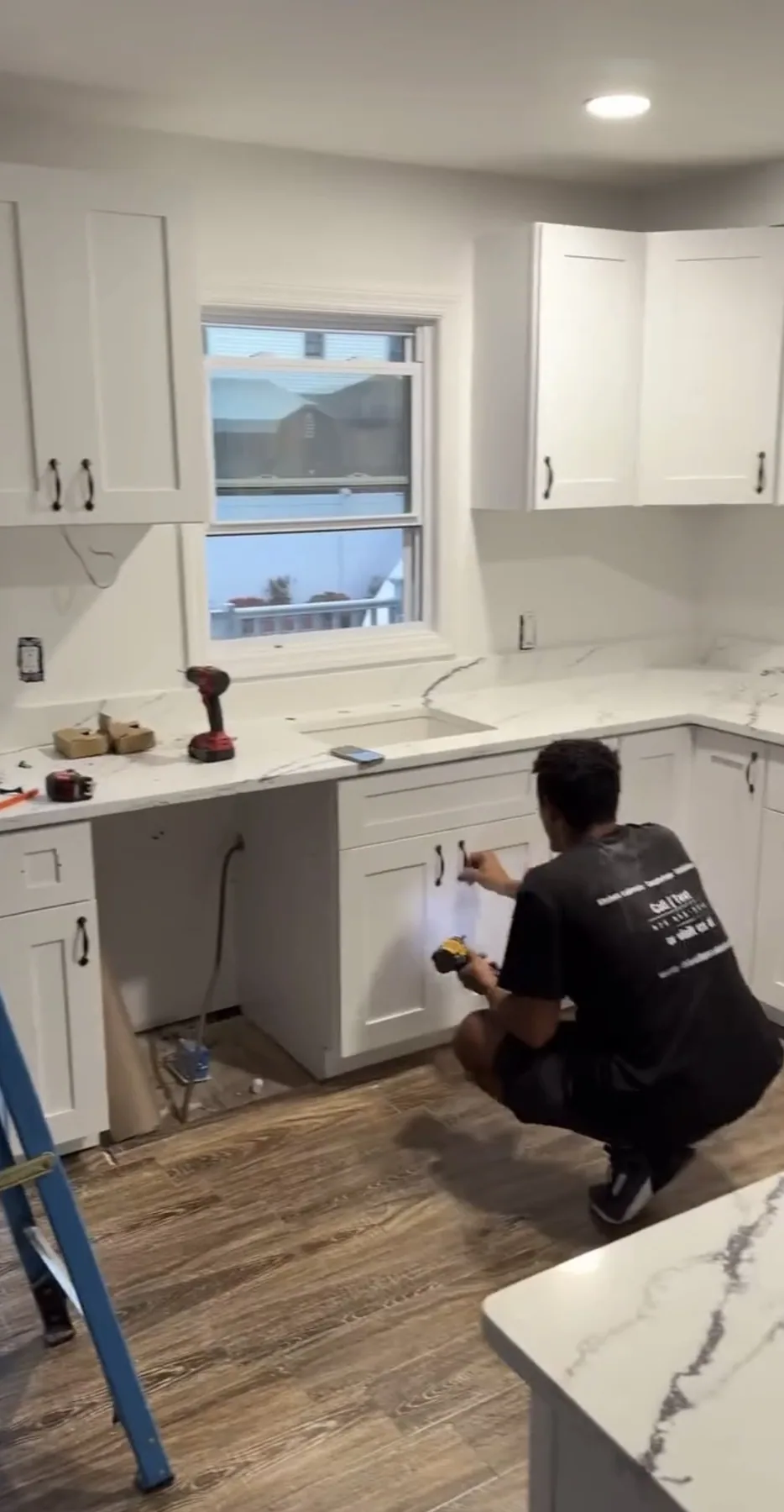 Installer kneeling to attach white shaker kitchen cabinets during installation