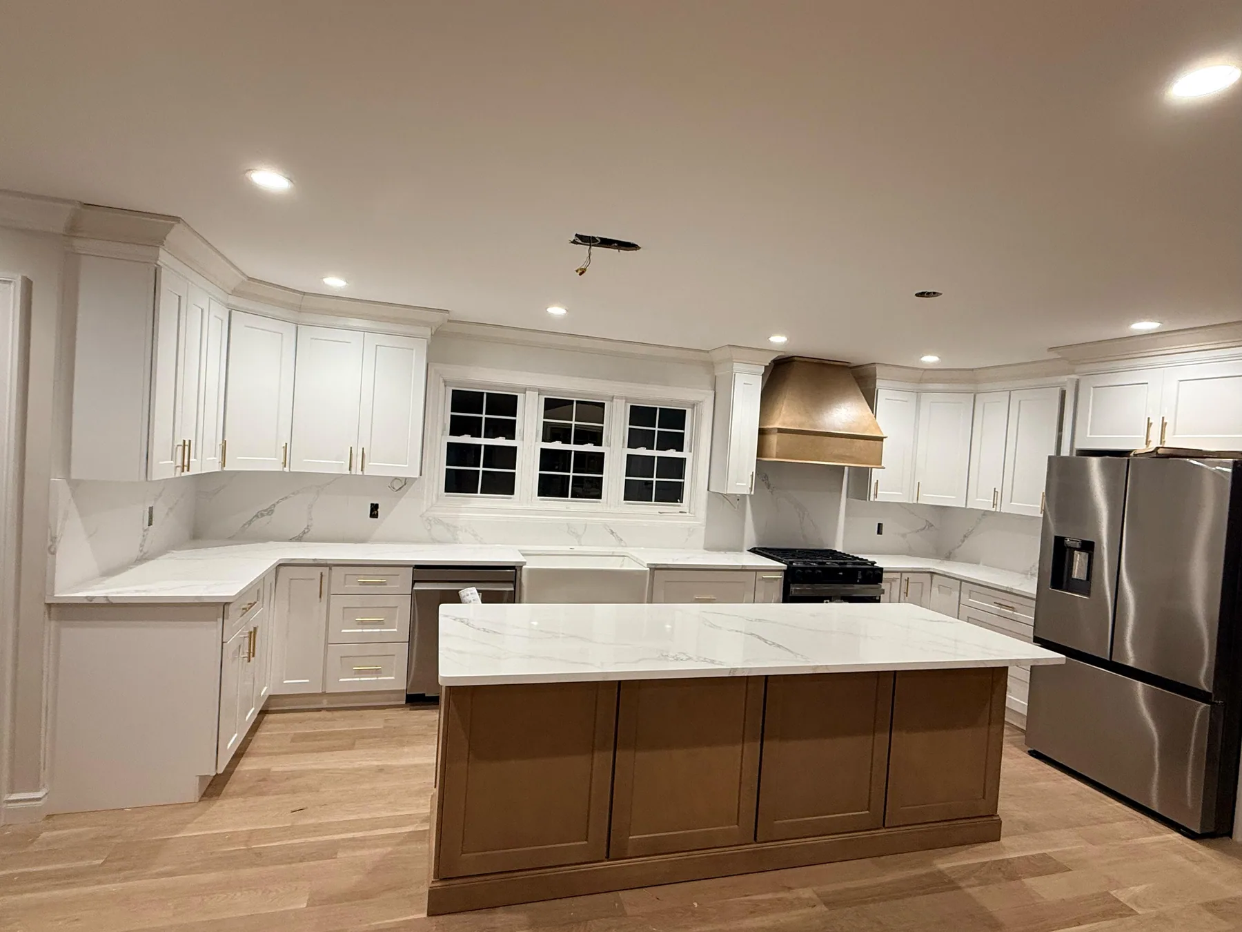 White kitchen cabinets with a warm wood island, marble countertops and stainless steel refrigerator