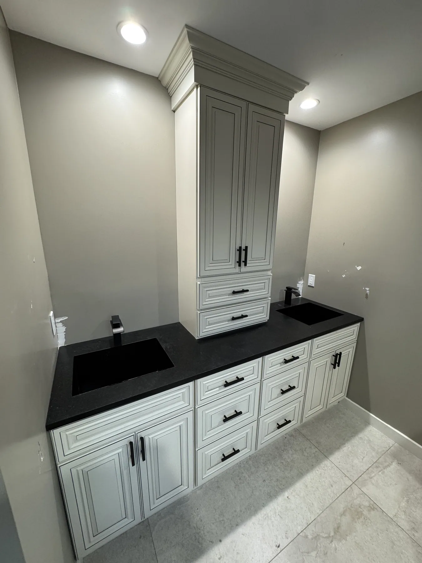 Close view of cream cabinet drawers with black pulls and a light stone floor