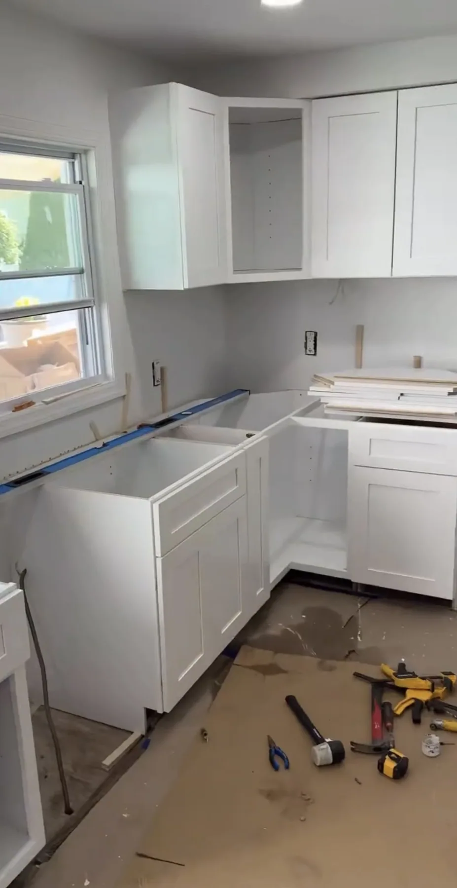 White kitchen cabinets partly installed with tools on the floor during installation