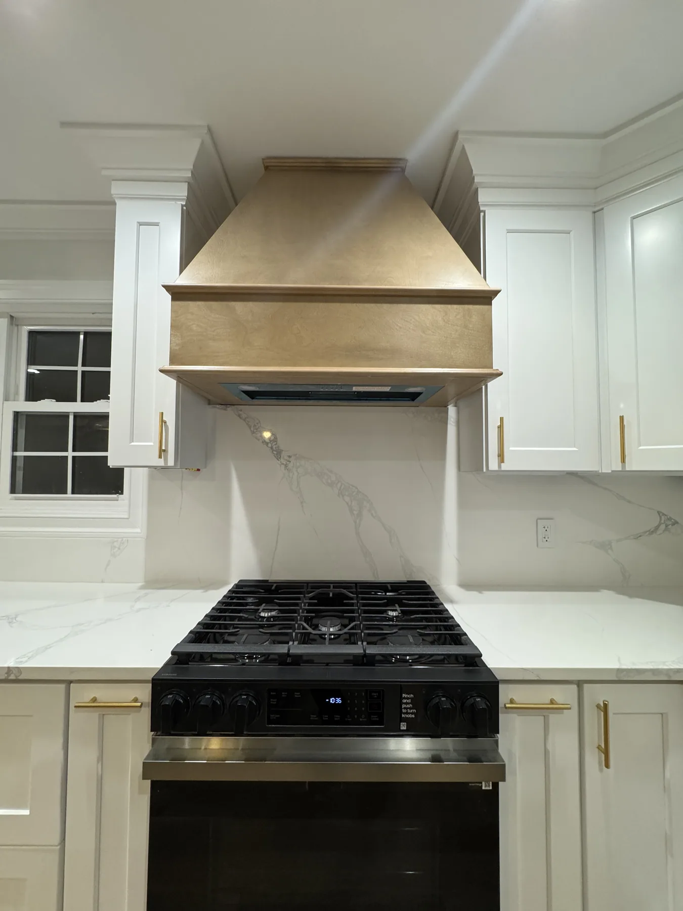 Wood range hood over a slide-in range between white cabinets with brass hardware