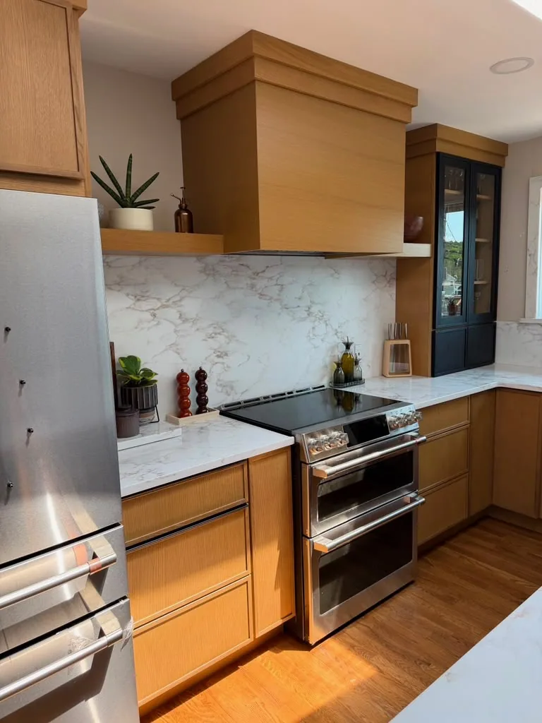 Wood range hood over a double oven range with a marble backsplash