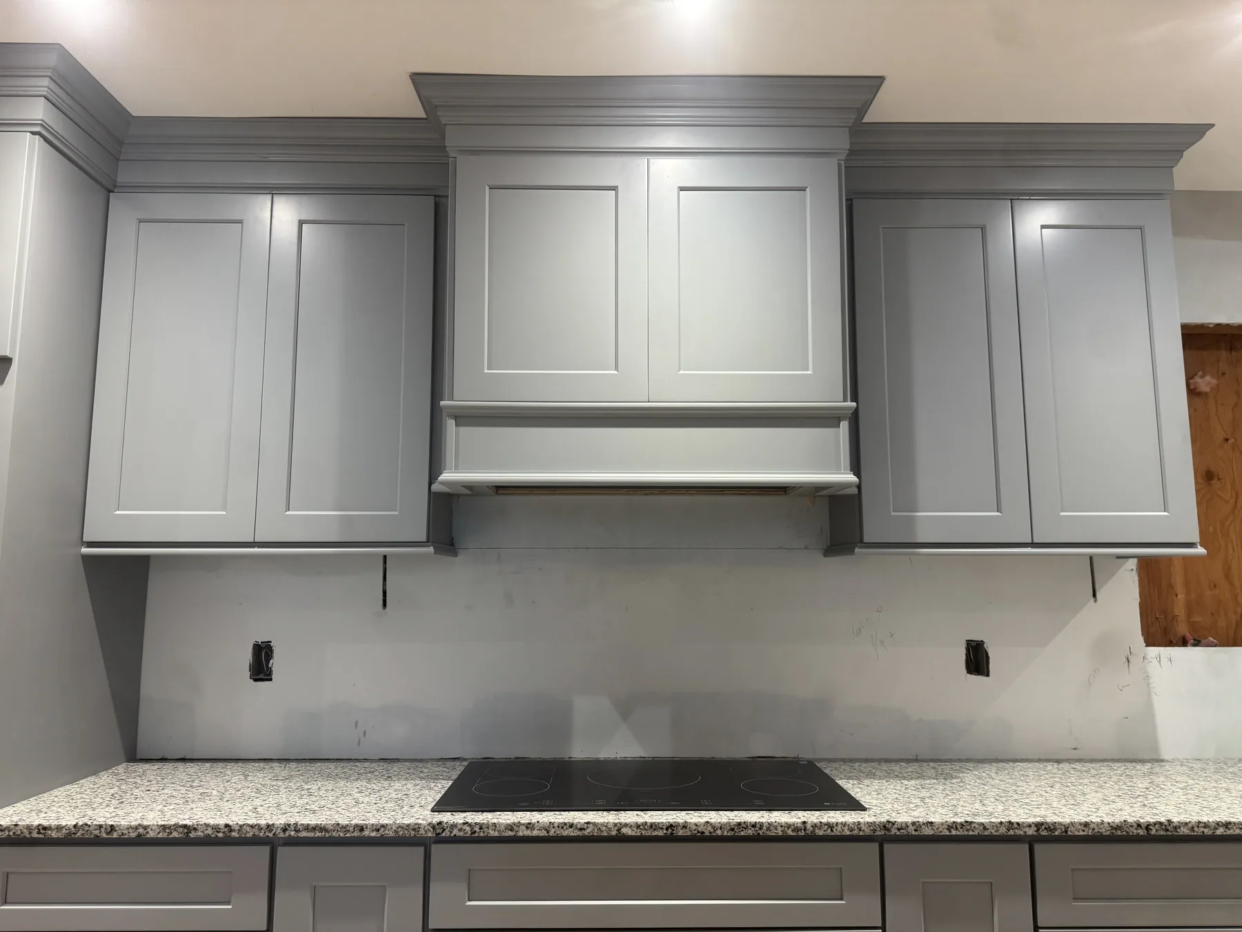 Gray kitchen cabinets with a hood surround and granite countertops