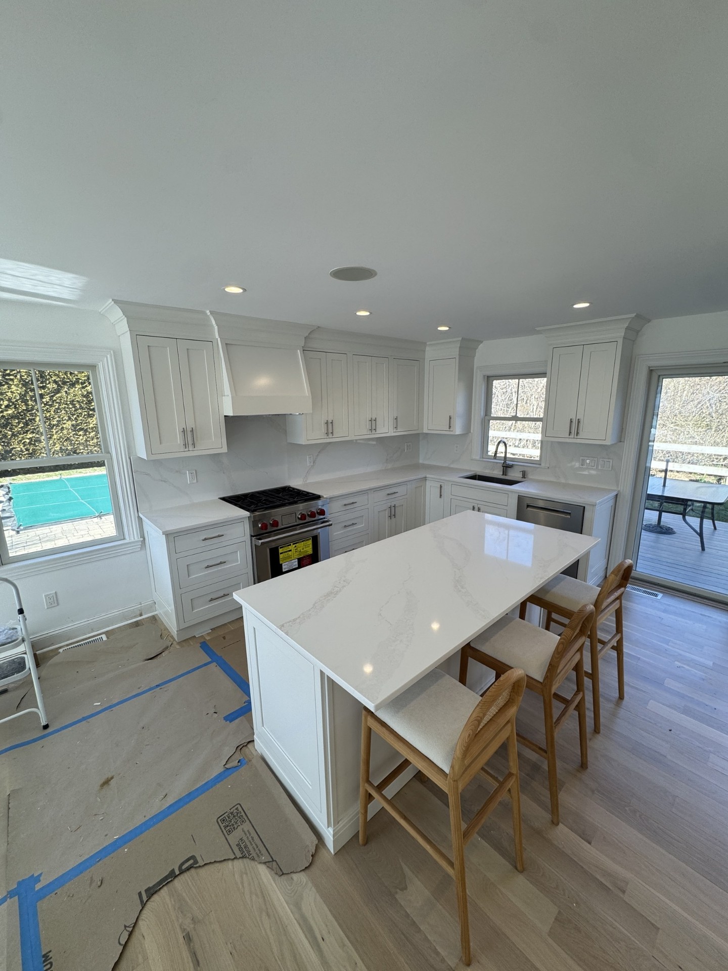 Bright all-white kitchen with large marble island and wood counter stools