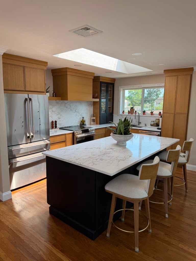 Warm oak kitchen with black island, marble backsplash, and skylight